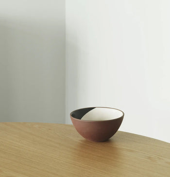 The Normann Copenhagen Line Bowl, 15cm, by Normann Copenhagen features a small, round ceramic shape with a matte brown exterior in red clay and a white-and-black divided interior—an artistic accent for any space.