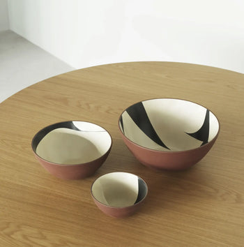 The Normann Copenhagen Line Bowl, 15cm, adds artistic flair to your round, light wood table with its maroon exterior and black-and-white abstract pattern inside.