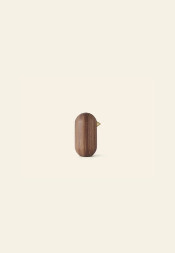 The Normann Copenhagen Little Bird, 10cm, is a minimalist dark wood figurine with a golden beak, showcased against a plain off-white background.