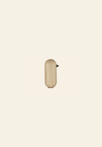 The Normann Copenhagen Little Bird, 13.5cm, features a minimalist wooden design with a smooth rounded body and small black beak, making a stylish decorative accent against a plain light beige background.