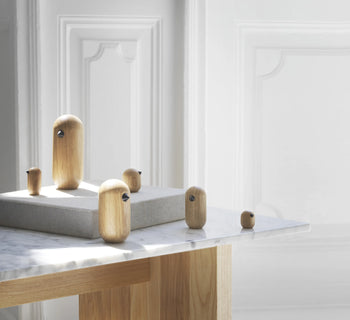 The Normann Copenhagen Little Bird, 7cm from Normann Copenhagen adds a minimalist touch to a bright room, displayed on a marble and wood table against white paneled walls for elegant home decor.