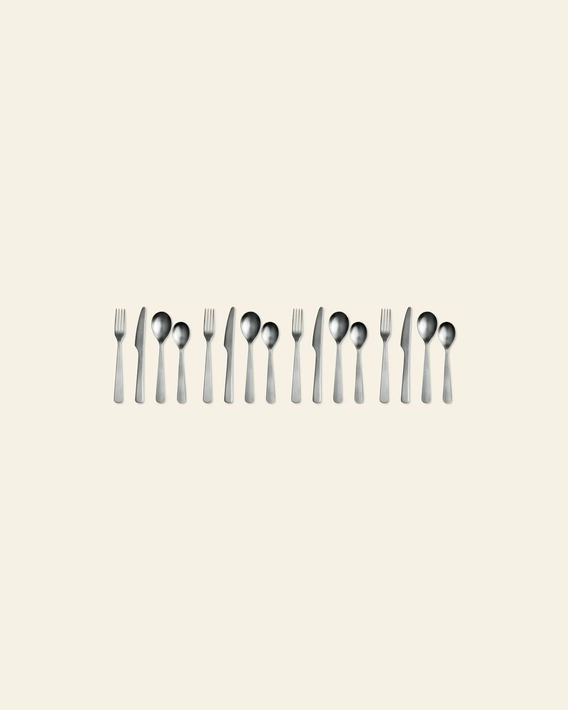 A set of Normann Copenhagen Cutlery Gift Box - 16 Pack by Normann Copenhagen is neatly arranged in pairs on a plain beige background, with the polished modern utensils evenly spaced and gleaming in the image.