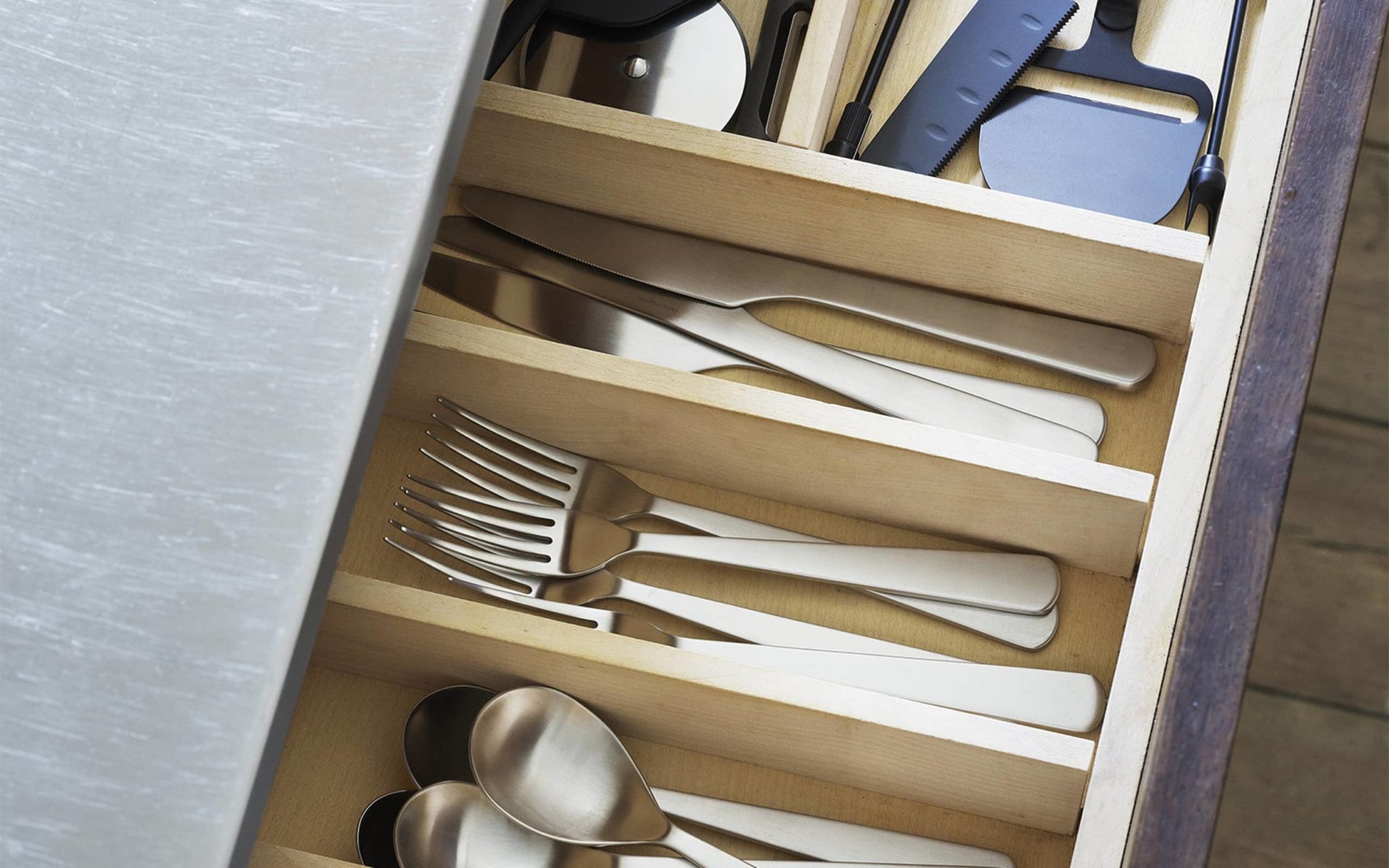 A polished wooden kitchen drawer is neatly organized with the Normann Copenhagen Cutlery Gift Box - 16 Pack, featuring separate compartments for forks, knives, and spoons by Normann Copenhagen, along with various utensils in the top section.