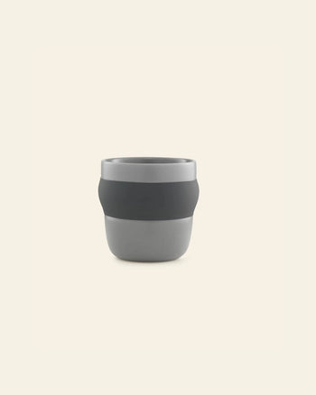 The Normann Copenhagen Obi Cup is a minimalist grey porcelain cup with a dark grey band, displayed against a light beige background.