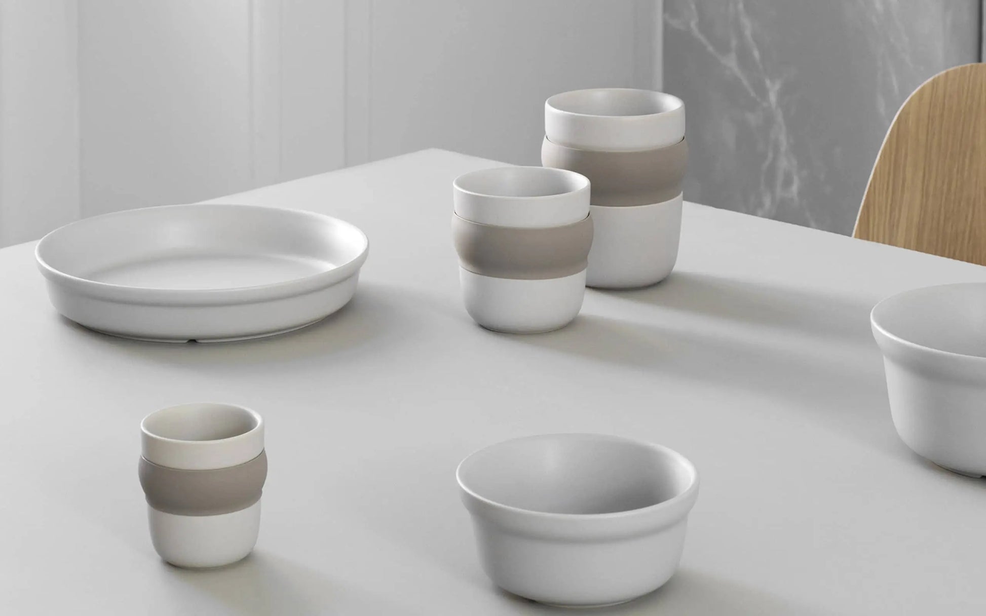 The Normann Copenhagen Obi Cup by Normann Copenhagen is displayed alongside matching bowls and a plate with subtle beige bands, all neatly arranged on a light gray table in a modern setting.