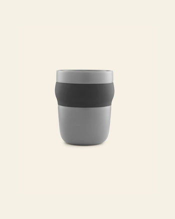 The Normann Copenhagen Obi Mug is a minimalist gray porcelain mug with a black band around the middle, displayed against a plain light beige background.