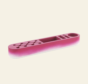 The Normann Copenhagen One Piece Organizer Classic, a pink and white rectangular tray with multiple compartments, circular cutouts, and a geometric design on one end, is shown against a plain cream background.