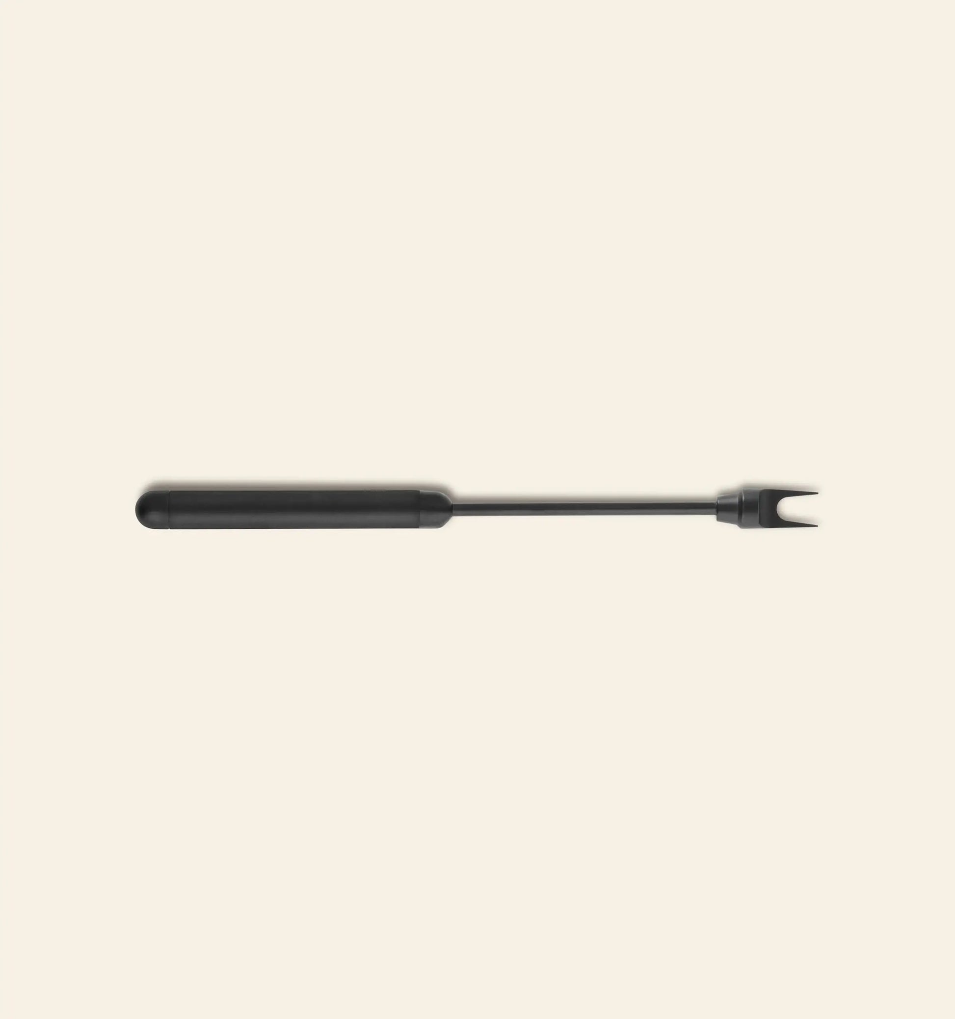 The Normann Copenhagen Pebble Cheese Fork, a black two-pronged fork with a long handle, is centered on a plain light beige background.