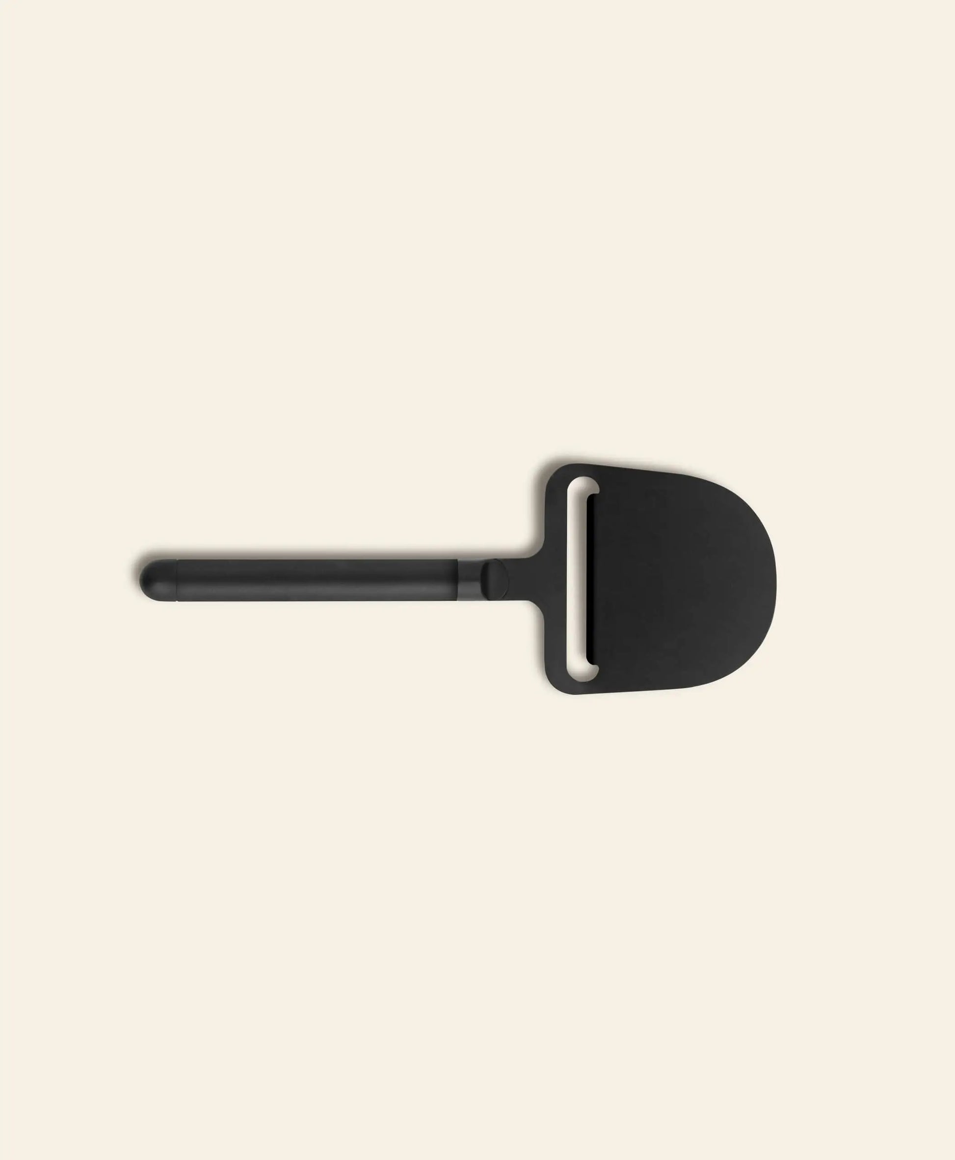 The Normann Copenhagen Pebble Cheese Plane by Normann Copenhagen showcases a sleek black, wide blade and straight handle, ideal for smooth cheese serving, displayed on a plain light beige background.