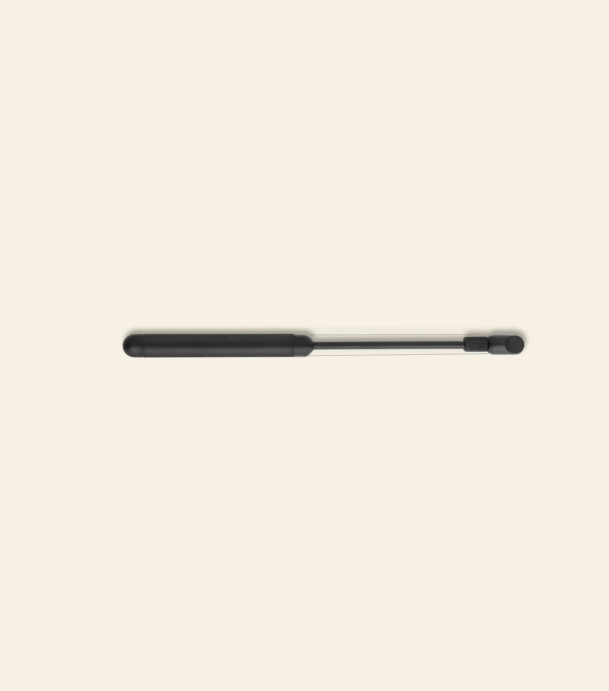 A black and silver gas strut, echoing the sleek look of the Normann Copenhagen Pebble Cheese Slicer, lies horizontally on a light beige background with its thicker black end to the left.