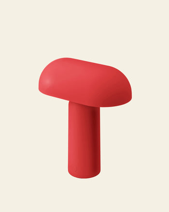 The Normann Copenhagen Porta Table Lamp is a red, mushroom-shaped portable lamp with a smooth top and cylindrical stem, showcasing modern design by Normann Copenhagen against a plain light beige background.