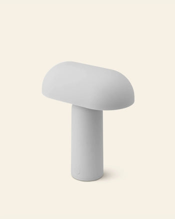 The Normann Copenhagen Porta Table Lamp by Normann Copenhagen features a minimalist, modern mushroom-inspired design with a rounded top and cylindrical base—an ideal portable lamp for contemporary decor lovers.