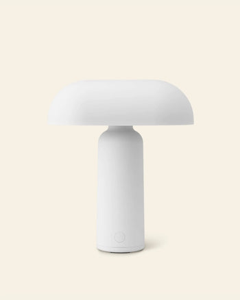 The Normann Copenhagen Porta Table Lamp features a modern minimalist design, with a dome-shaped shade and cylindrical base by Normann Copenhagen, shown against a plain light beige background.