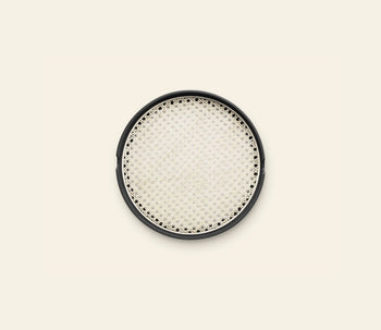 The Normann Copenhagen Salon Tray, 35cm, features a round black frame and a woven light-colored bamboo mesh center, shown against an off-white background.