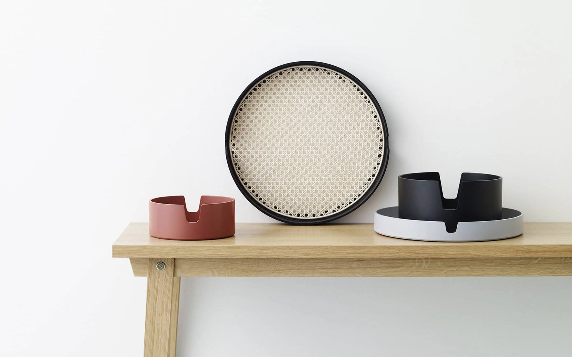 A minimalist wooden shelf displays a 35cm Normann Copenhagen Salon Tray and two modern pet bowls—one reddish-brown, one black with a white base—set against a plain white wall.