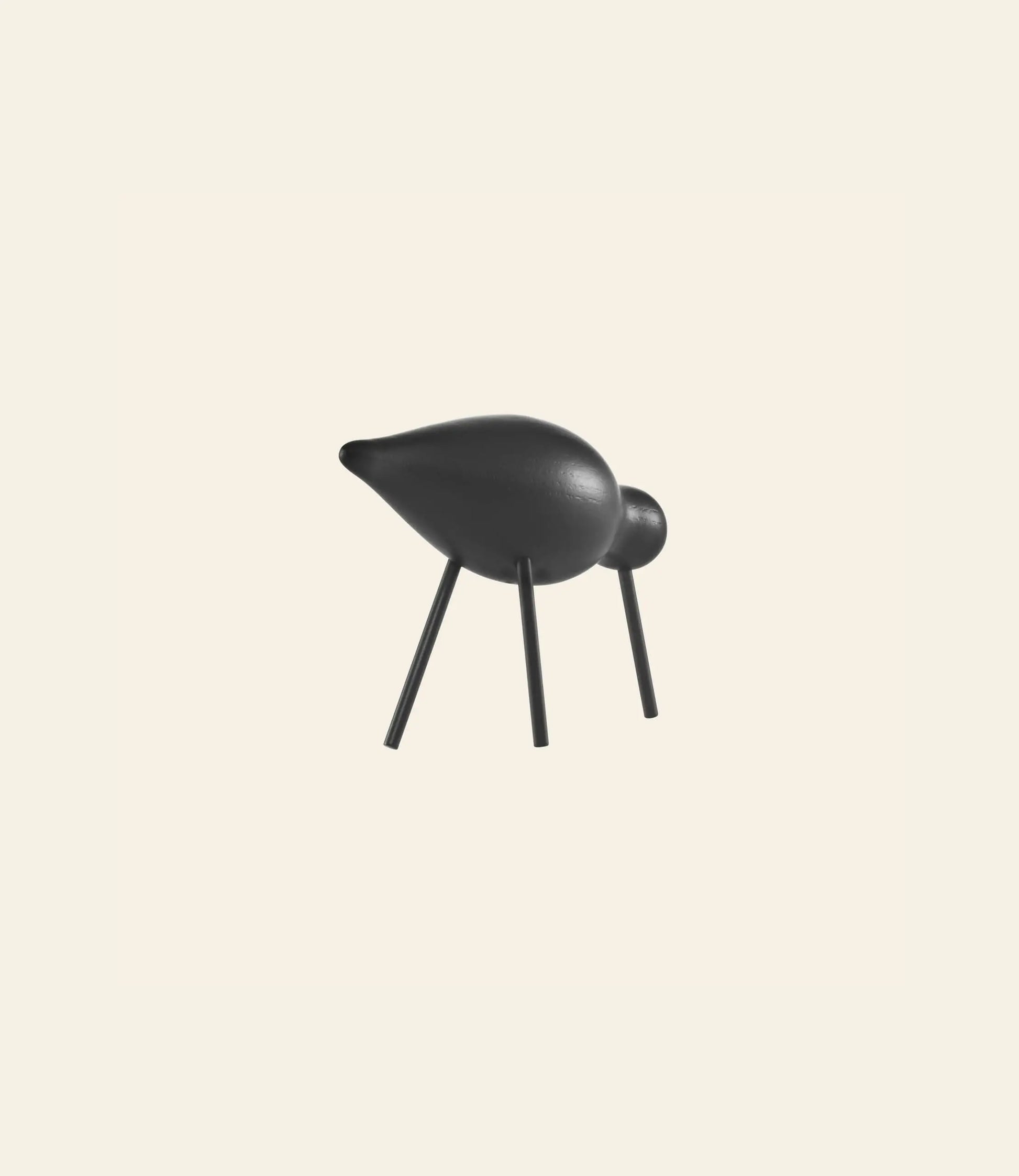 The Normann Copenhagen Shorebird Medium Oak by Normann Copenhagen is a minimalist black sculpture with four stick-like legs, a round head, and an elongated body, inspired by oak wood and minimalist design against a plain light background.