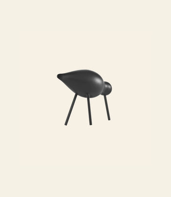 The Normann Copenhagen Shorebird Medium Oak by Normann Copenhagen is a minimalist black sculpture with four stick-like legs, a round head, and an elongated body, inspired by oak wood and minimalist design against a plain light background.