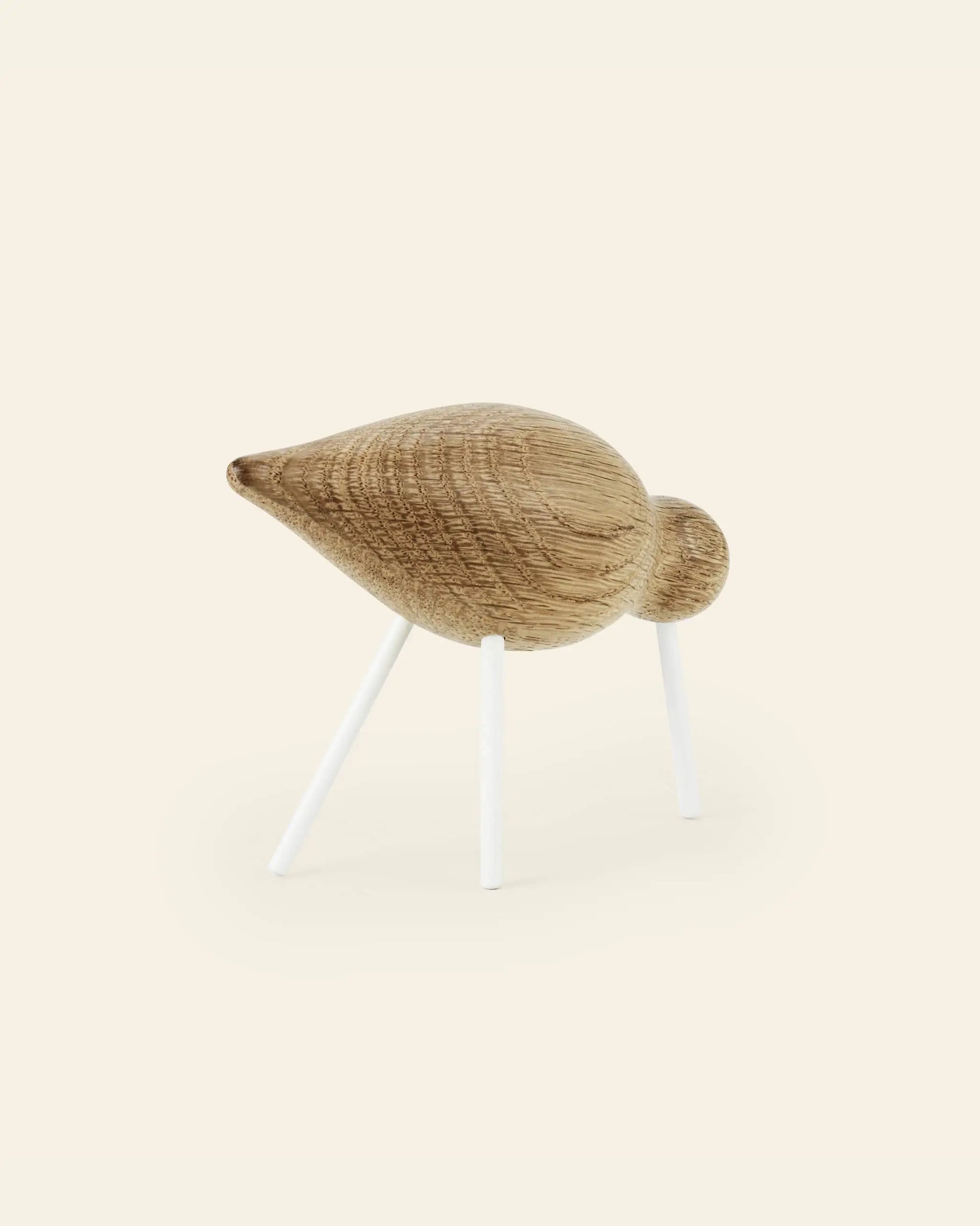The Normann Copenhagen Shorebird Medium Oak is a minimalist figurine crafted from oak with a smooth finish, standing on three slim white legs, reflecting modern design by Normann Copenhagen.