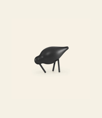 The Normann Copenhagen Shorebird Small Oak is a minimalist black figurine with a smooth, rounded body and angled oak legs, designed by Normann Copenhagen, displayed against a plain off-white background.