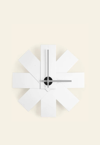 The Normann Copenhagen Watch Me Wall Clock by Normann Copenhagen features overlapping white rectangular panels in a starburst pattern, minimalist black hands, and a black center, creating a modern statement for home decor.