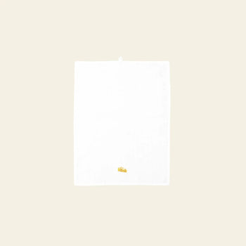 The Normann Copenhagen Yummy Tea Towel by Normann Copenhagen, made from linen and cotton, is shown on a light beige background with a small embroidered yellow wedge of cheese near the bottom edge.