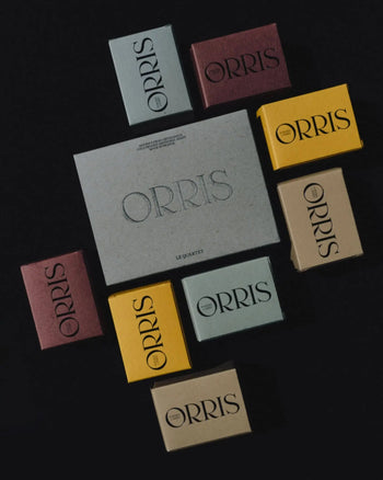 A flat lay of nine colorful ORRIS soap boxes encircling a larger gray box, all against a black background. Discover ORRIS Le Quartet: face and body cleansing bars with skincare benefits.