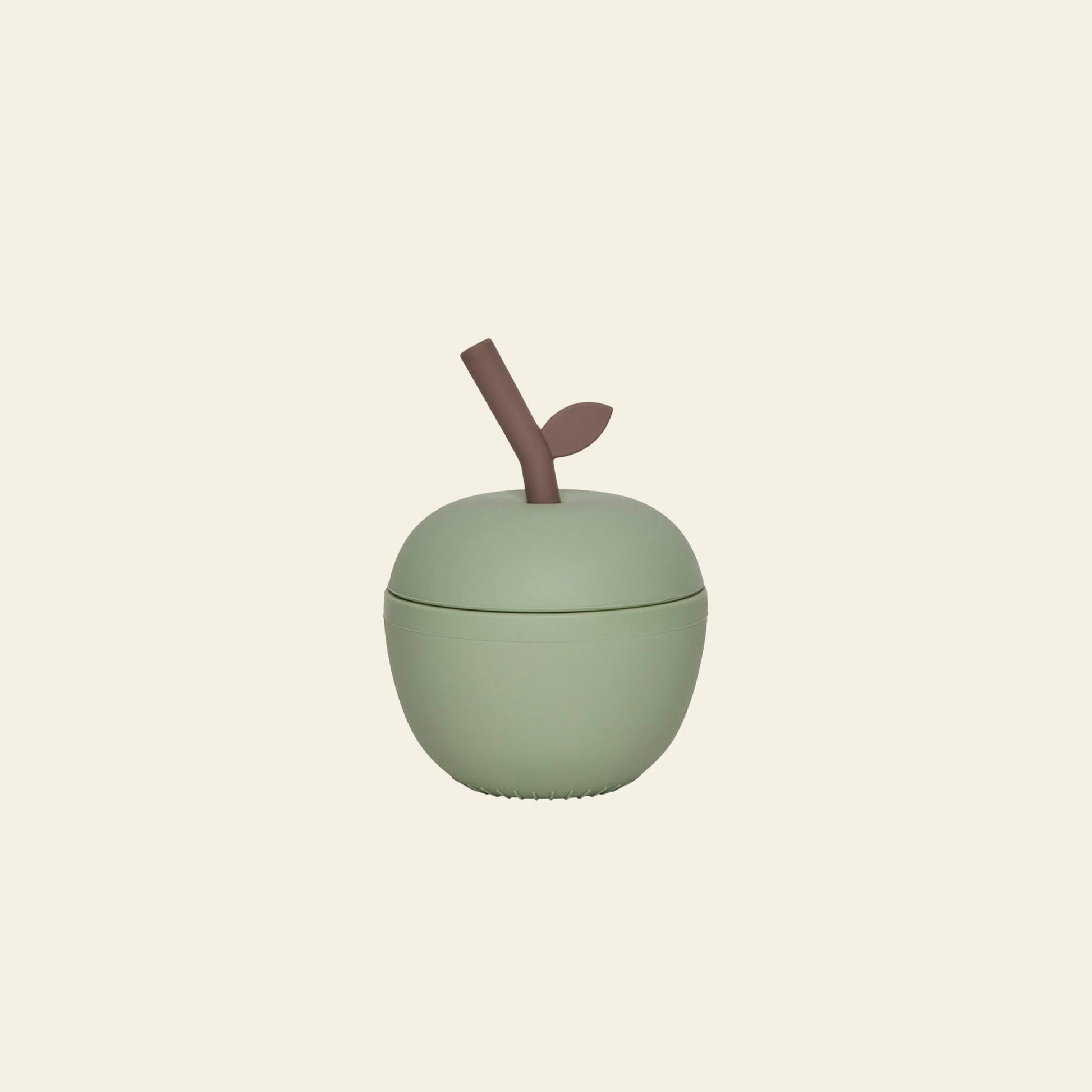 The OYOY Living Design Apple Cup - Green is a light green, apple-shaped silicone kids cup with a brown stem and leaf, from OYOY Living Design, pictured on a plain beige background—ideal for childrens drinks.