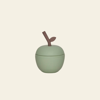 The OYOY Living Design Apple Cup - Green is a light green, apple-shaped silicone kids cup with a brown stem and leaf, from OYOY Living Design, pictured on a plain beige background—ideal for childrens drinks.