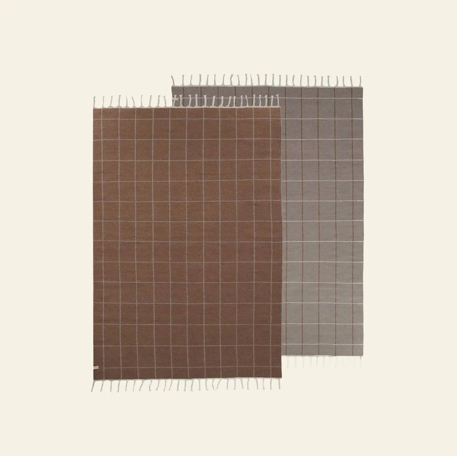 Two reversible OYOY Living Design Grid Rugs—one brown, one gray—feature white lines and short fringe. Displayed overlapping on a light background, they add modern style to any space.