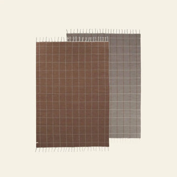 Two reversible OYOY Living Design Grid Rugs—one brown, one gray—feature white lines and short fringe. Displayed overlapping on a light background, they add modern style to any space.