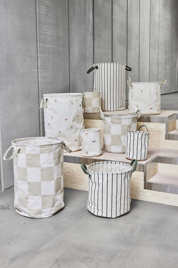 The OYOY Living Design Moira Laundry & Storage Basket, Medium, by OYOY Living Design, features playful animal prints and patterns with handles—ideal for organizing a childs room. Displayed on wooden steps against a concrete wall.