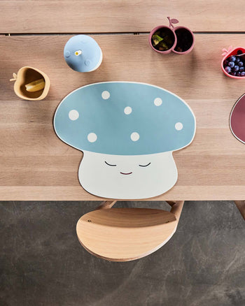 A wooden table set with a blue and white OYOY Living Design Mushroom Cup, small apple- and pear-shaped bowls filled with fruit and snacks, a wooden chair, and a cheerful, child-friendly atmosphere.