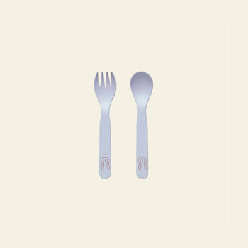 A white fork and spoon with rounded edges from the OYOY Living Design Pullo Cutlery Set are side by side. Each handle features a pink bunny face illustration. The eco-friendly PLA set rests on a pale cream background.