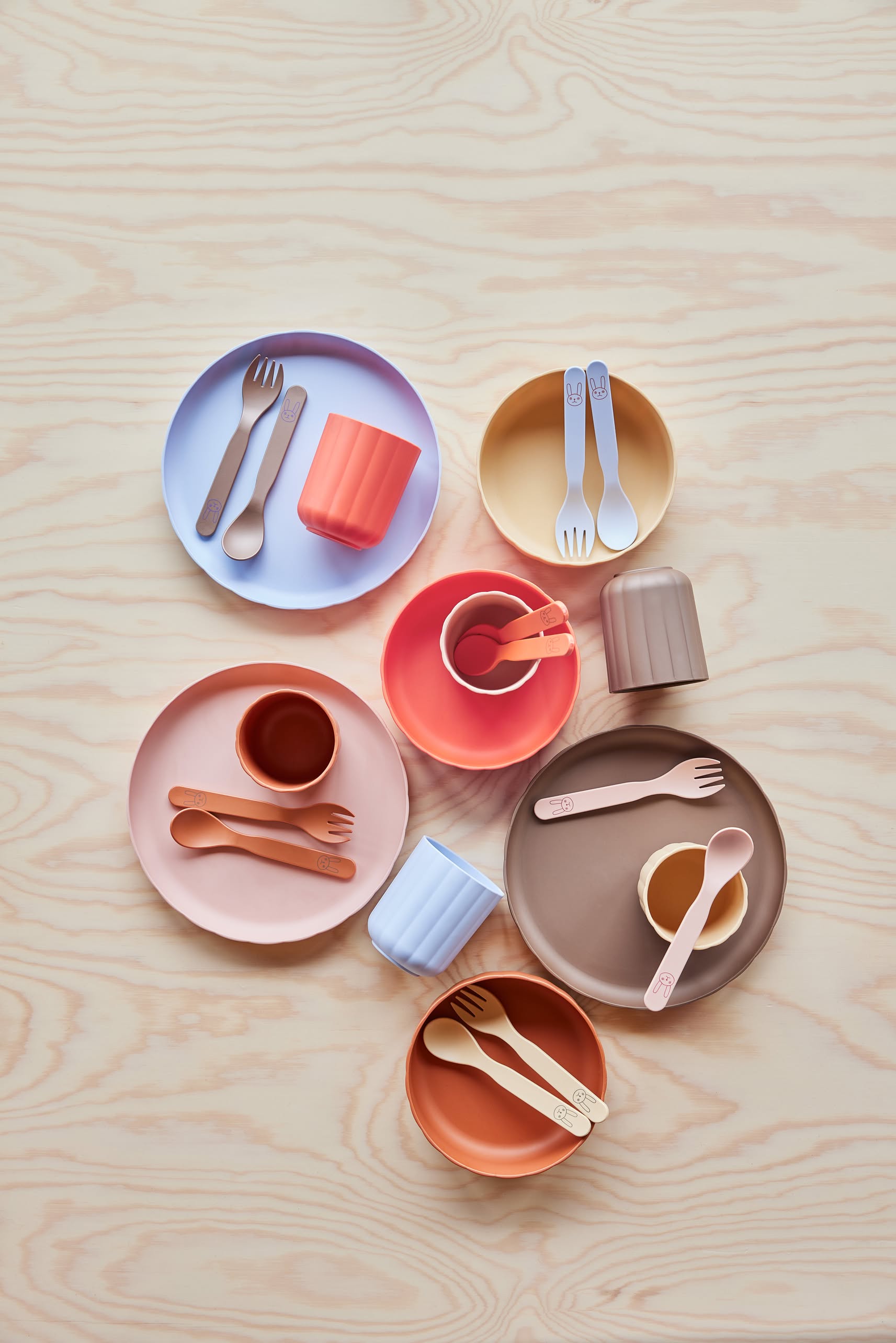 OYOY Living Design Pullo Cutlery Sets, made from eco-friendly PLA, display a range of pink, orange, brown, yellow, purple, and blue on a light wood surface—perfect colorful tableware for toddlers by OYOY Living Design.