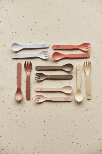 A flat lay of ten OYOY Living Design Pullo Cutlery Sets, crafted from eco-friendly PLA in neutral shades, each set includes a spoon and spork with bunny faces, arranged on a beige surface with small colored dots.