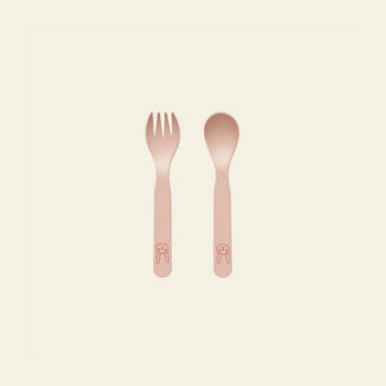 The OYOY Living Design Pullo Cutlery Set by OYOY Living Design is a pink toddler fork and spoon set made from eco-friendly PLA, with simple animal face drawings on the handles, placed side by side on a light background.
