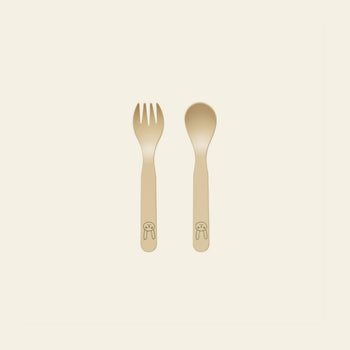 The OYOY Living Design Pullo Cutlery Set for toddlers features a beige fork and spoon made from eco-friendly PLA, rounded handles, and a cute bunny face near the base, displayed on an off-white background.