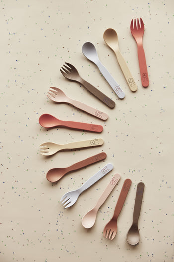 OYOY Living Design Pullo Cutlery Set toddler sporks, made from eco-friendly PLA and featuring cute animal faces on the handles, are artfully arranged in a curve on a speckled beige background.