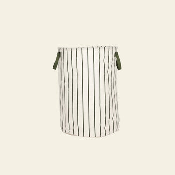 The OYOY Living Design Raita Laundry & Storage Basket (Medium) features a cylindrical shape in white fabric, elegant vertical black stripes, and two green handles, displayed against a plain beige background.