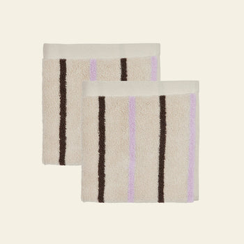 Two beige OYOY Living Design Raita Wash Cloths, made from organic cotton terry with vertical brown and light purple stripes, are shown side by side on a plain light background. Sold as a pack of 2.
