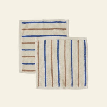 The OYOY Living Design Raita Wash Cloth, Pack of 2, features two organic cotton terry wash cloths with brown and blue stripes—one horizontal, one vertical—on a cream background.