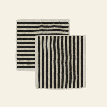 The OYOY Living Design Raita Wash Cloth, Pack of 2, features organic cotton terry cloths with black and white stripes—one horizontal, one vertical—each bordered in white and displayed side by side on a plain background.