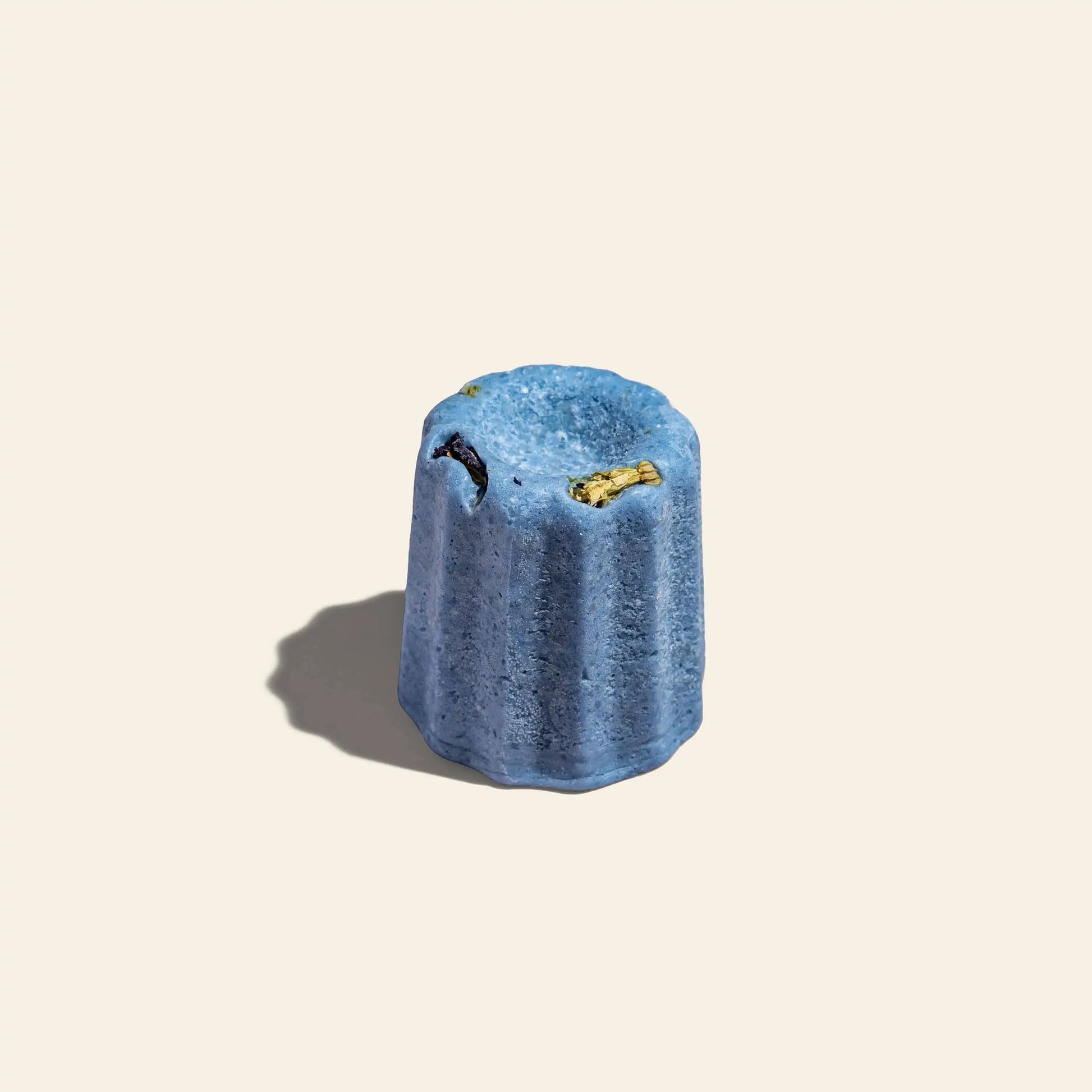 A single Oasis Beauty Kitchen Blue Pea Lemongrass Solid Shampoo, Midi Canele, with fluted edges and a blue hue, sits on a light beige background. A soft shadow to the left hints at its lemongrass inspiration.