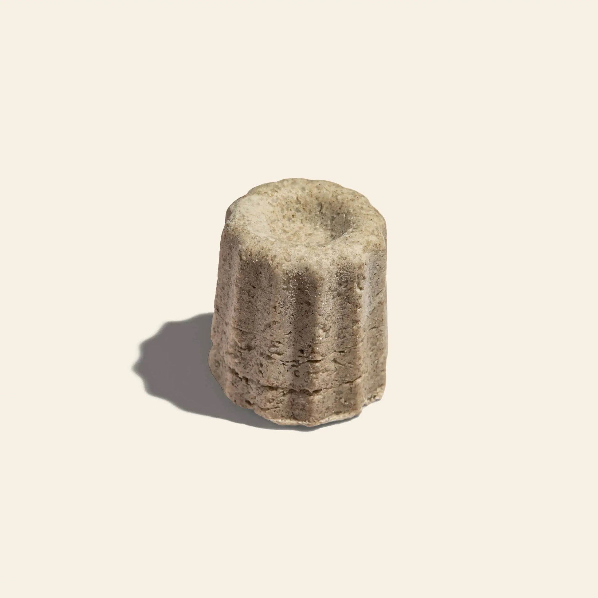 A single, small, ribbed, canele-shaped Oasis Beauty Kitchen Ginger Solid Shampoo sits on a plain light background—evoking natural remedies with the power of ginger to help reduce hair loss.