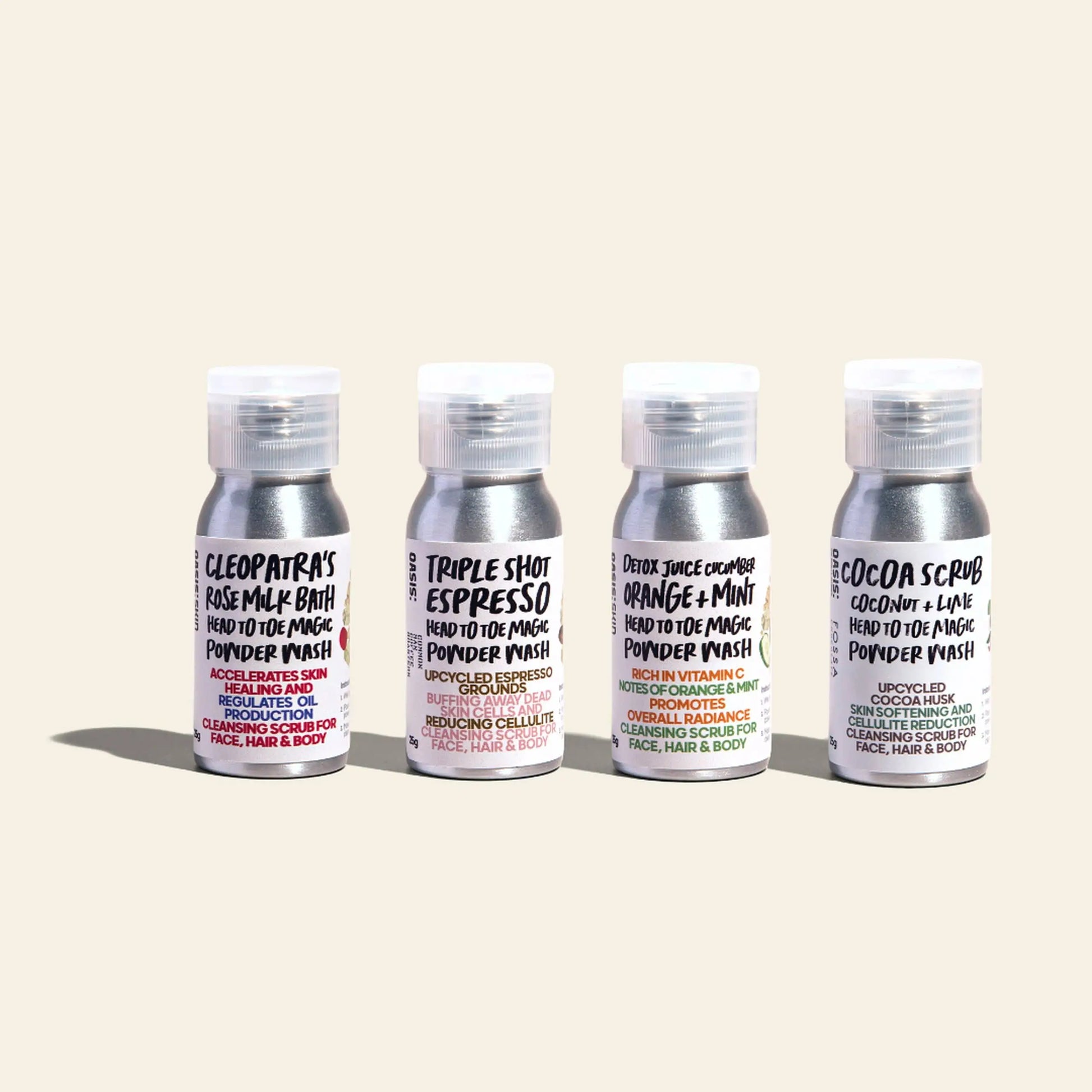 Four 25g bottles of Oasis Beauty Kitchen Head to Toe Magic Powder Wash, a vegan, plant-based cleanser, are arranged side by side in Rose Milk Bath, Triple Shot Espresso, Orange + Mint, and Cocoa Scrub scents on a light background.