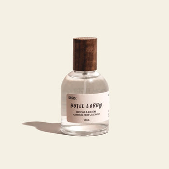 A small clear bottle with a wooden cap labeled Oasis Beauty Kitchen Room and Linen Mist, 50ml stands on a beige background, casting a shadow to the left. Enjoy this refreshing, perfume-grade mist with a subtle fresh linen scent from Oasis Beauty Kitchen.