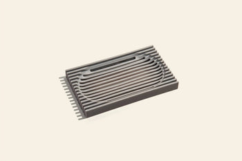 The Oasis Beauty Kitchen The Lattice Soap Dish by Oasis Beauty Kitchen features a modern rectangular design with durable metallic construction and parallel grooves, perfect for organizing soaps on a light beige background.