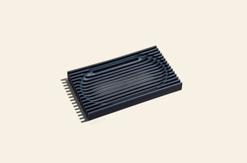 The Oasis Beauty Kitchen The Lattice Soap Dish by Oasis Beauty Kitchen features a black rectangular design with raised curved and straight ridges, crafted for durability and ideal for everyday zero waste living. Photographed on a plain beige background.
