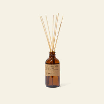 The P.F. Candle Co. 3.5oz Reed Diffuser - Amber & Moss features a brown glass bottle with a kraft label, filled with fragrance oils and several natural-colored diffuser sticks, set against a plain, light background.