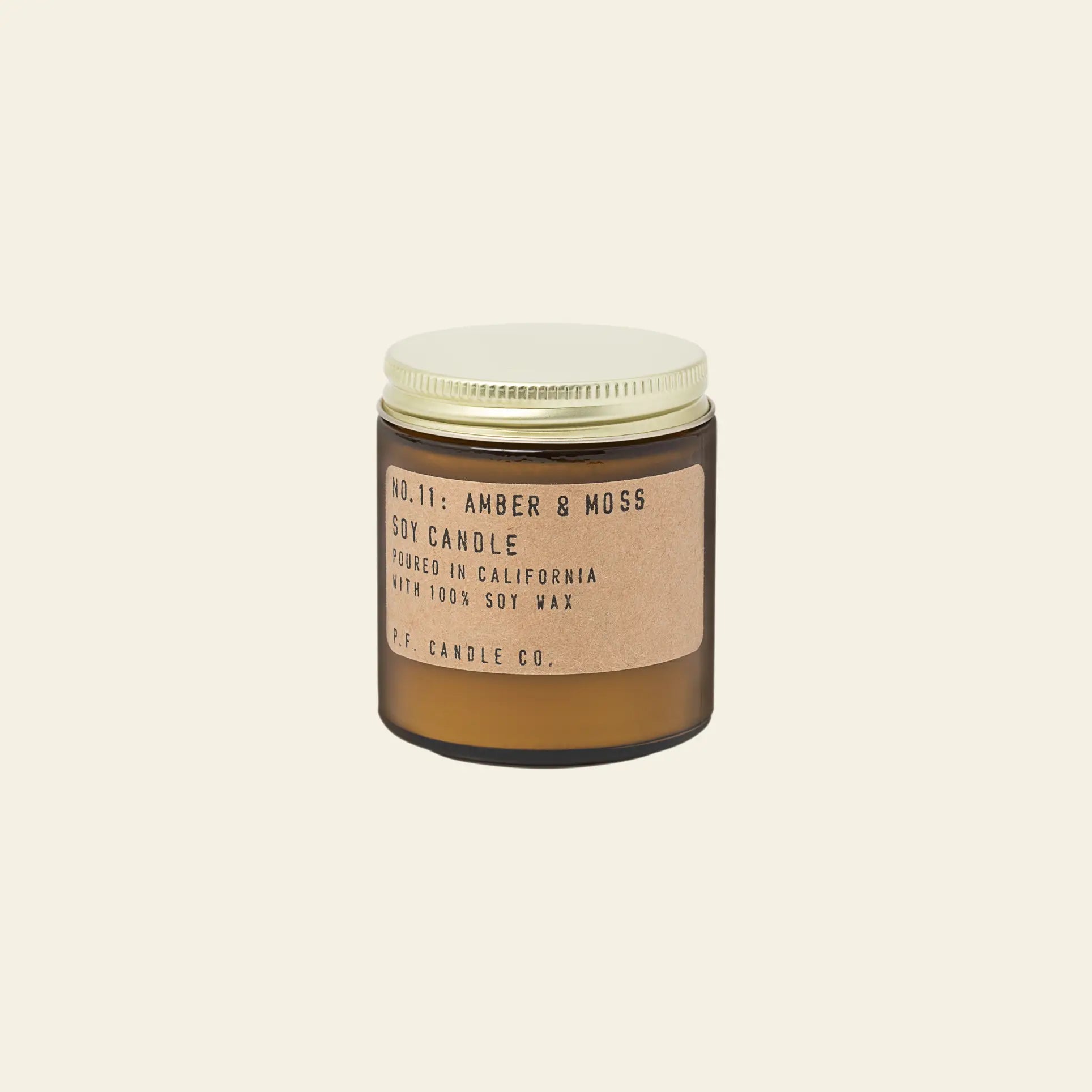 The P.F. Candle Co. No. 11 Amber & Moss 3.5 oz Mini Candle comes in a brown glass jar with a gold lid, featuring sage and lavender notes and a label stating it’s poured in California with 100% soy wax by P.F. Candle Co.